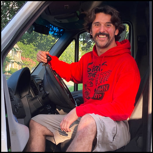 Lifestyle shot of Woody in his #MotoVan, showcasing the red One Down Five Up Hoodie.